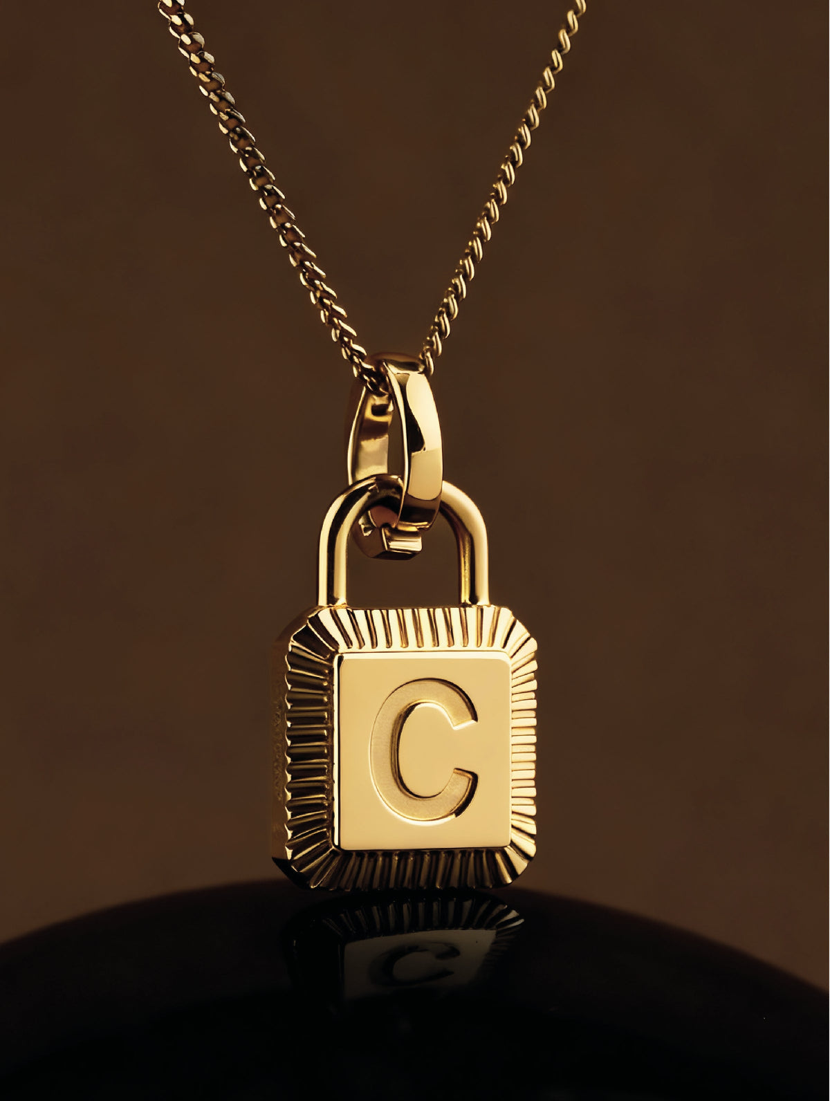 Gold lock-shaped pendant with a letter 'C' on a dark background